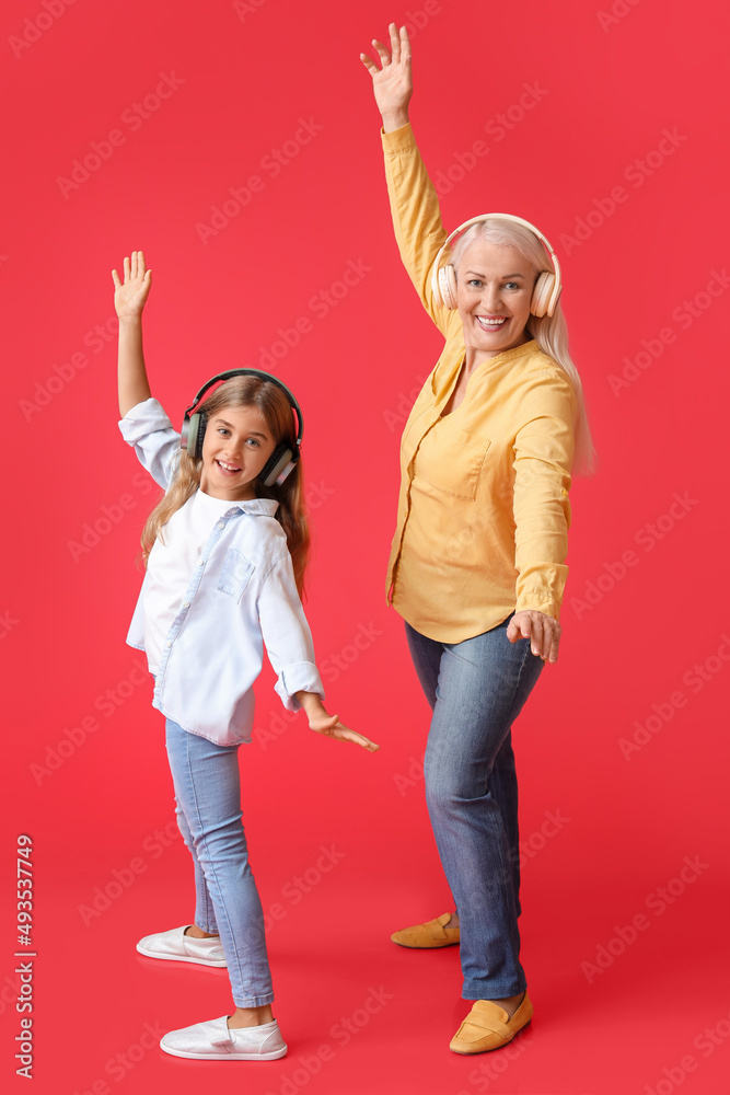 Little girl and her grandma in headphones dancing on red background Little girl and her grandma in headphones dancing on red background