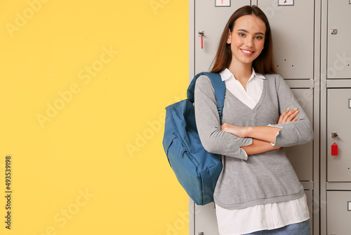 Obraz na plátně Female student near locker on yellow background