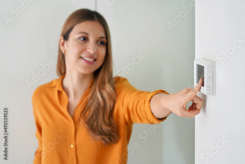 Lowering the temperature for energy saving. Young woman adjusting digital central heating thermostat at home. Focus on the hand.