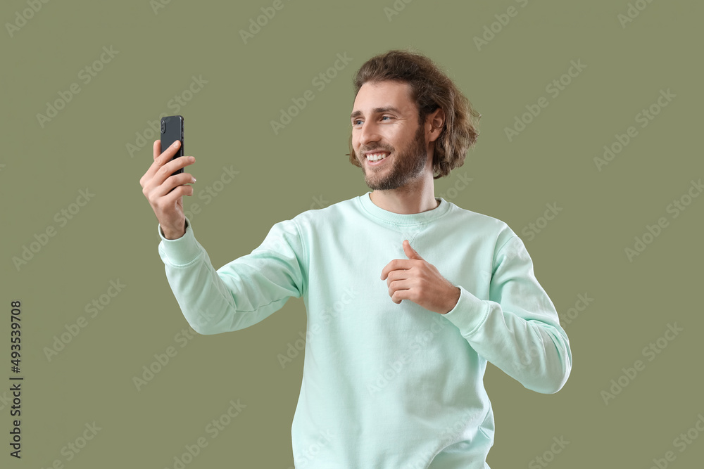 Handsome man with mobile phone taking selfie on green background Handsome man with mobile phone taking selfie on green background