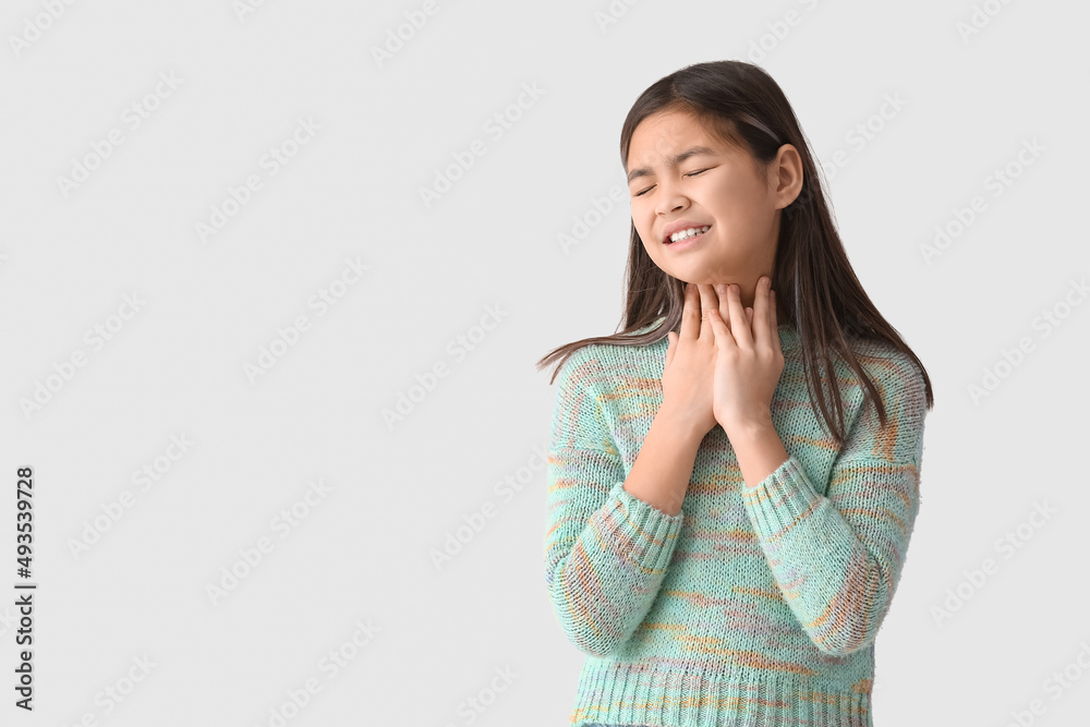Ill Asian girl with sore throat on light background Ill Asian girl with sore throat on light background