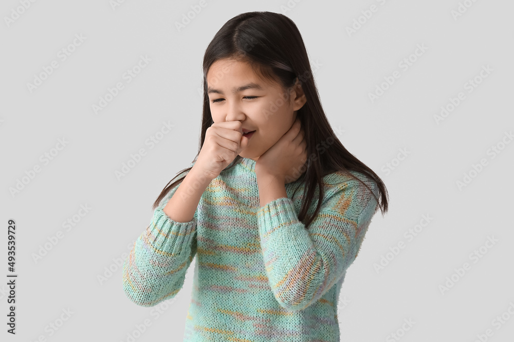 Ill Asian girl with sore throat on light background Ill Asian girl with sore throat on light background