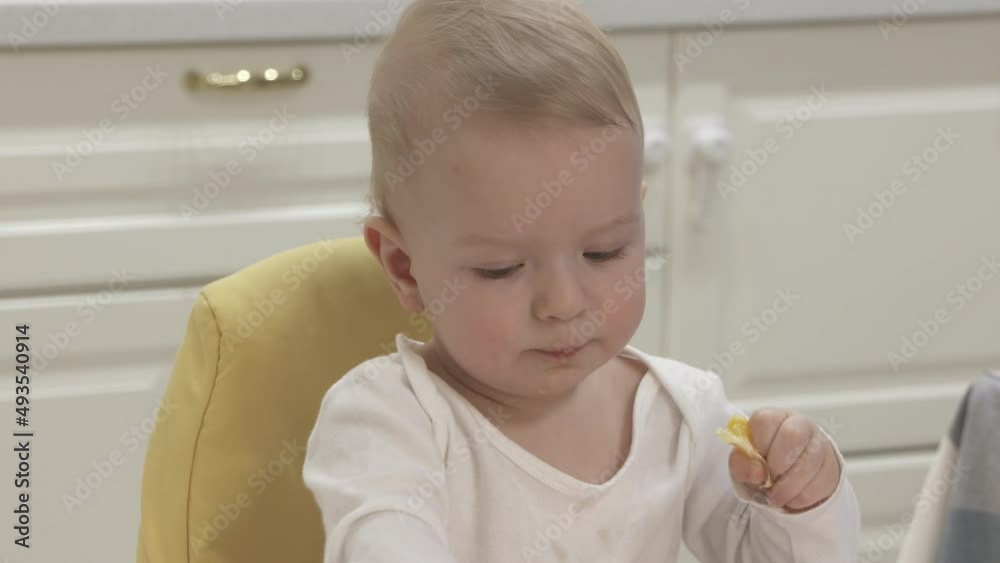 Baby boy with citrus fruit sitting on high chair for babies, one-year-old baby boy eating tangerine. High quality 4k footage Baby boy with citrus fruit sitting on high chair for babies, one-year-old baby boy eating tangerine. High quality 4k footage