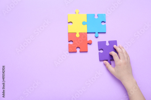 Child with puzzle pieces on lilac background. Concept of autistic disorder
