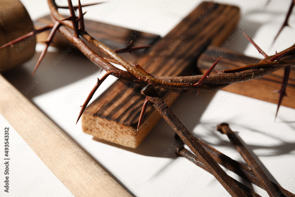 Crown of thorns with wooden cross and nails on light background, closeup
