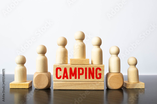 Camping word on a wooden cube sign with a blurry background of a campsite in the summer