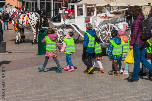Fototapeta Naklejka Na Ścianę i Meble -  A group of small children dressed in spring clothes and putting off yellow reflective safety vests so they can be easily seen by drivers. Children safely walk the streets of the city