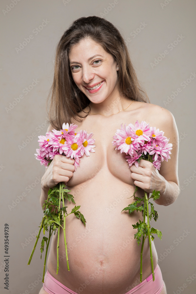 Portrait of a beautiful caucasian pregnant woman posing with flowers bouquet in hands in springtime and smiling to the camera. Maternity, Mother's Day Holiday concept. 