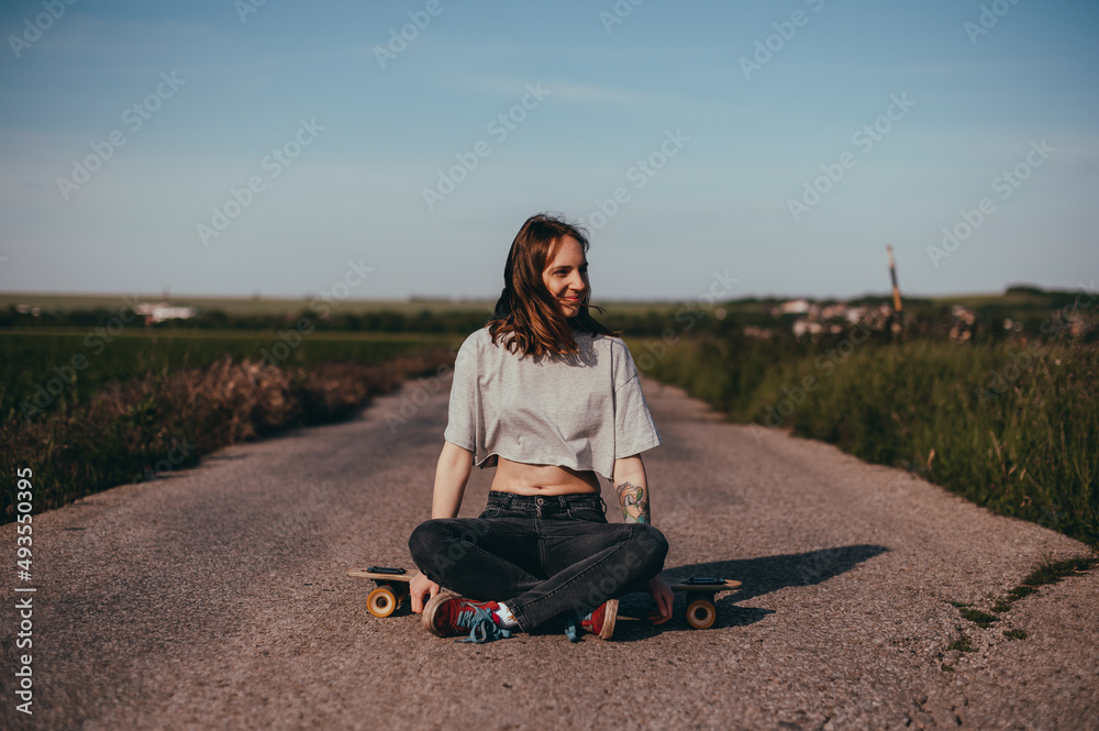portrait of a young woman sitting in the middle of the road alone on a longboard. 