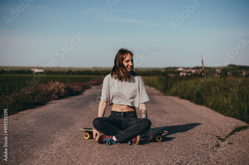 portrait of a young woman sitting in the middle of the road alone on a longboard.  © Big Shot Theory