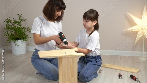 Happy family mother and daughter assembling wooden furniture together with screwdriver. DIY concept