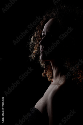 Side lit brunette girl with long curly hair, silhouette studio portrait on dark background