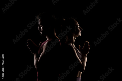 Fit couple posing together. Boy and girl praying back to back side lit silhouettes on black background. © Nikola Spasenoski