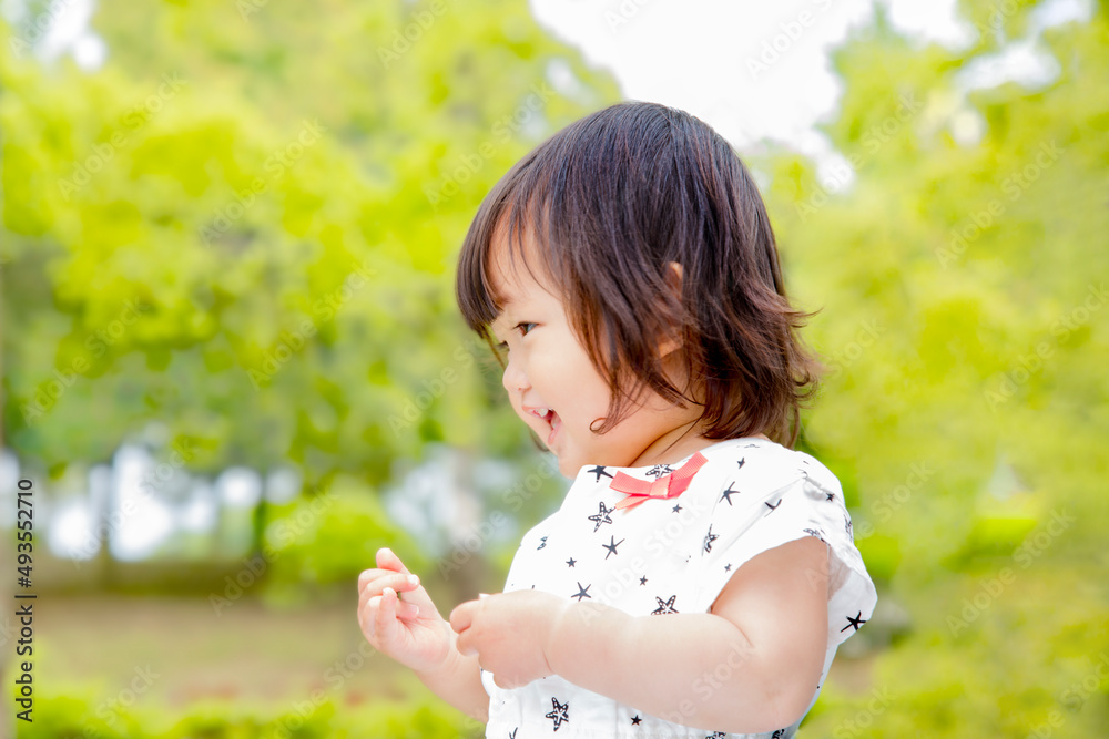 新緑の樹木を背景に笑顔で踊る幼い女の子。育児,教育,躾,愛情,幸せなイメージ