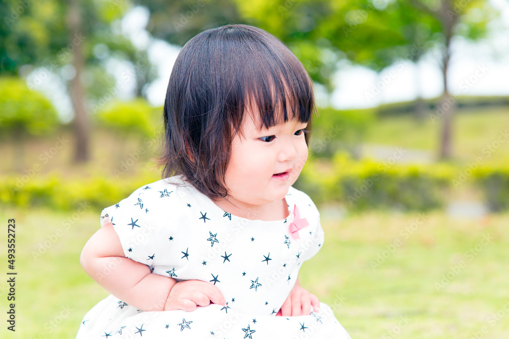 新緑の樹木を背景に興味深く下を観察する幼い女の子。育児,教育,躾,愛情,幸せなイメージ