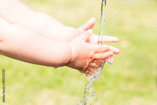 緑を背景に屋外の水道で手を洗う幼児の手のクローズアップ。手洗い,教育,躾,清潔のイメージ