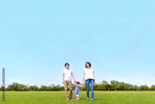 青空を背景に緑の芝の上で手を繋ぐカメラ目線の幸せな娘と若いカップル。家族,幸せ,愛情,育児のイメージ