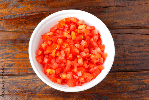 Fotografie Raw chopped and diced tomatoes cubes in ceramic bowl over rustic wooden table