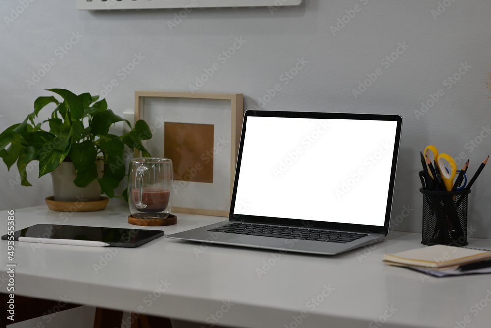 White modern office table with laptop with blank white screen, tablet, coffee cup and note books with no people, for business and technology concept.