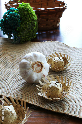 Garlic bulbs and straw hats on the jute fabric with wicker basket and dried flowers.