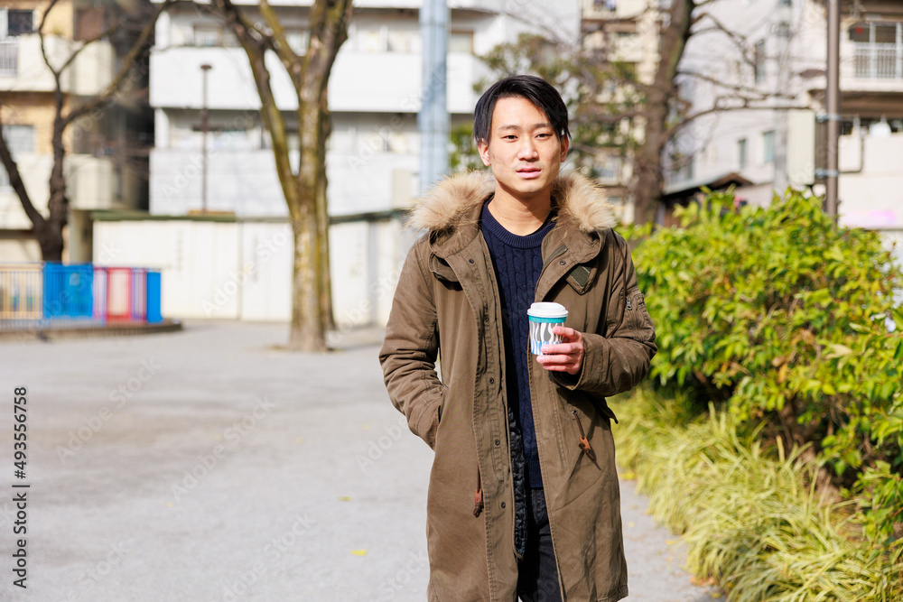 コーヒーのカップを片手に歩く若い男性 コーヒーのカップを片手に歩く若い男性