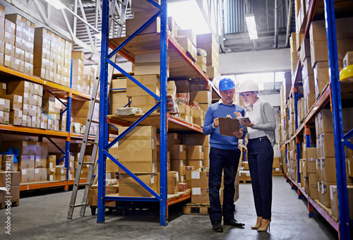 We know where every order is in this warehouse. Shot of a man and woman inspecting inventory in a large distribution warehouse. photo