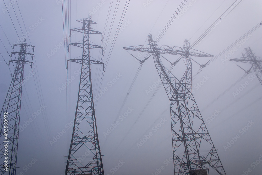 Towering electrical power pylons disappearing into thick fog landscape Towering electrical power pylons disappearing into thick fog landscape