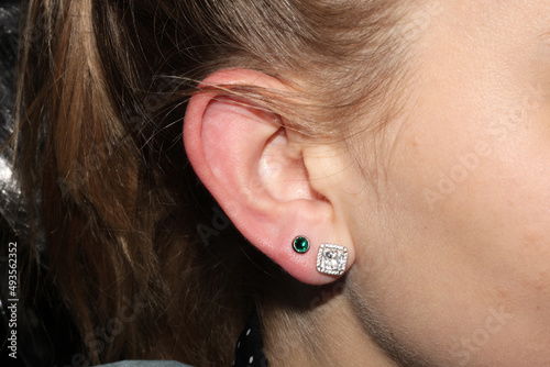 Girl's earlobe piercing. Double puncture. Beautiful earrings with white and emerald crystals. photo