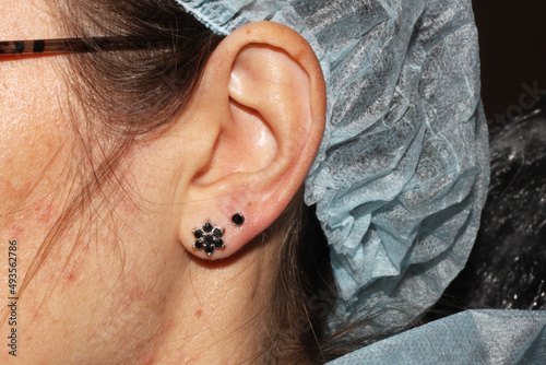 Girl's earlobe piercing. Double puncture. Beautiful earrings with white and black crystals. photo