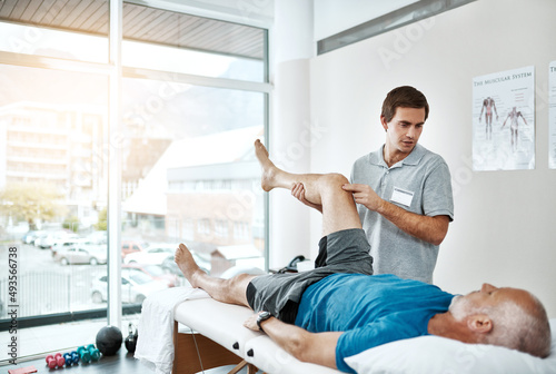 Gentle movements. Shot of a young male physiotherapist helping a client with leg exercises whos lying on a bed.