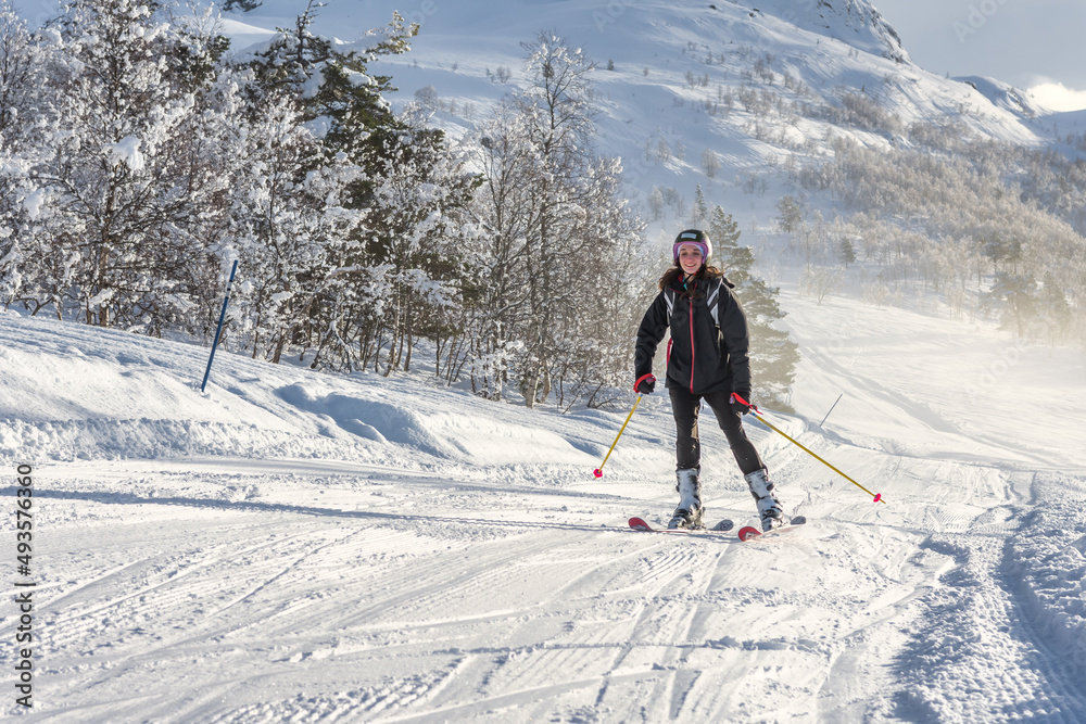Woman with brown hair smiling, wearing ski wear and a backpack skiing down a mountain in ski centre stryn, norway, horizontal