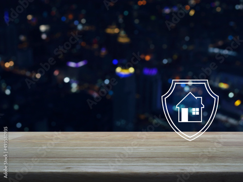 House with shield flat icon on wooden table over blur colorful night light modern city tower and skyscraper, Business home insurance and security concept