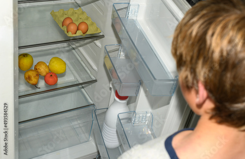 Child opens half-empty refrigerator. Concept of poverty, few resources and hunger