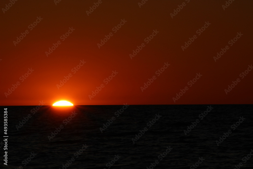 Solnedgang hvor solen kun lige har en lille bue over havoverfladen, som er helt sort