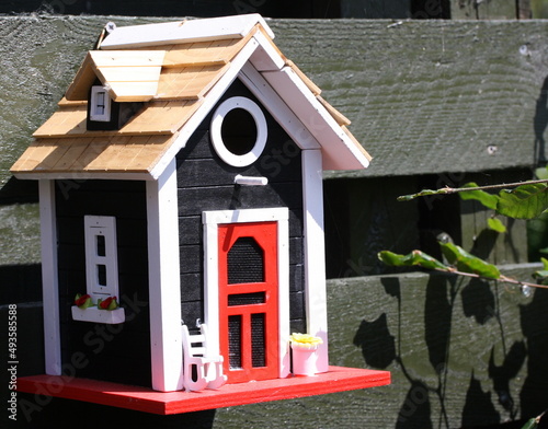 Fuglehus udformet som en lille hytte med rød hoveddør og kvist på taget photo