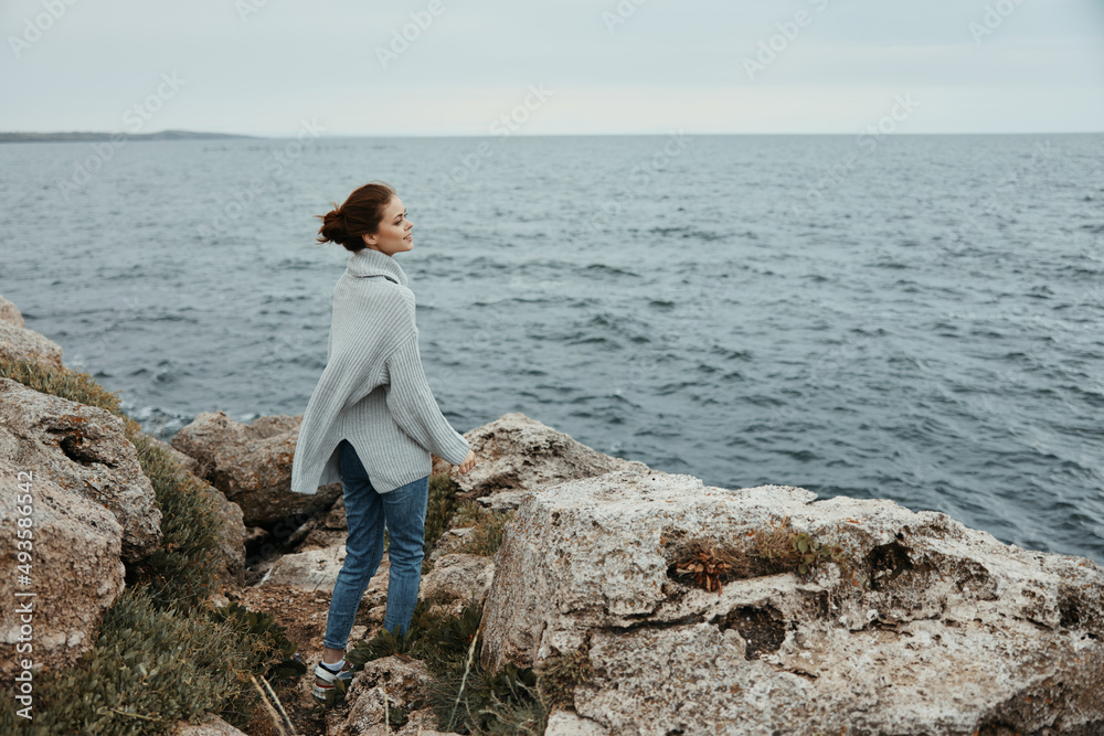 portrait of a woman in a gray sweater stands on a rocky shore nature female relaxing