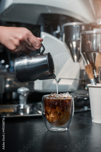 Ice coffee on a black table with cream being poured into it showing the texture and refreshing look of the drink