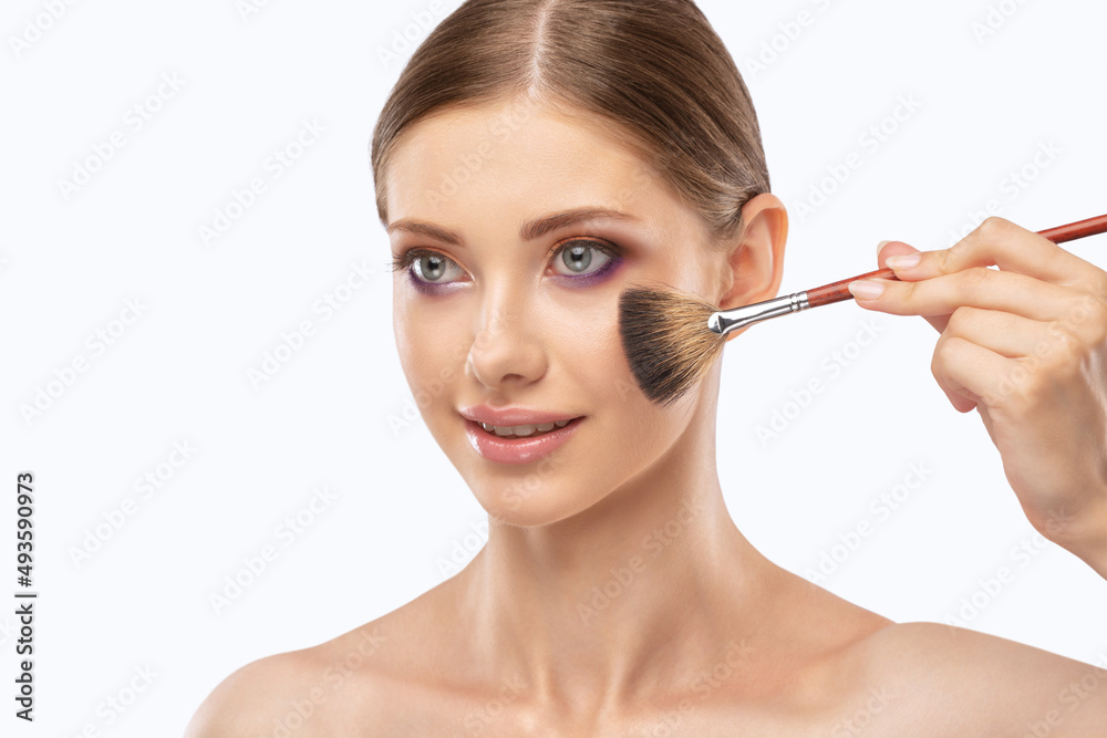 Portrait of a beautiful brunette girl with beautiful fresh makeup and healthy clean skin.Makeup artist holds a powder brush in her hands. Professional makeup concept