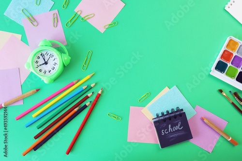 Stationery and alarm clock, pencils, pastel colored paper, on a green background, top view, the concept of learning, education, back to school, holidays