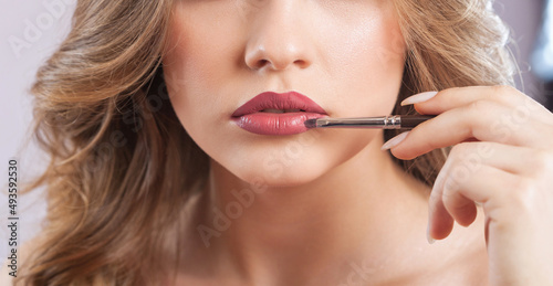 Portrait of a beautiful woman with curly blonde hair, beautiful fresh make-up and with healthy clean skin. Make-up artist does lips make-up.Professional makeup and cosmetology skin care.