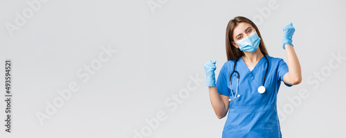 Covid-19, preventing virus, health, healthcare workers and quarantine concept. Cheerful optimistic female nurse winning, celebrating victory, fist pump upbeat, smiling in medical mask and gloves