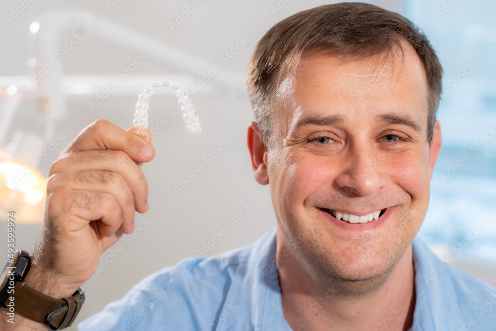 Smiling orthodontist doctor holds transparent aligners in his hands Smiling orthodontist doctor holds transparent aligners in his hands