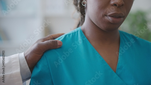 Male physician touching female colleague's shoulder, sexual harassment at work place photo