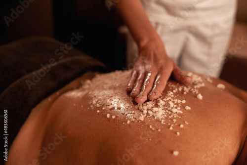 Female masseur do salt scrub on girl back in spa