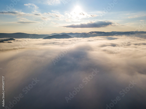 Flight over fog in Ukrainian Carpathians in summer. Mountains on the horizon. A thick layer of fog covers the mountains with a continuous carpet. Aerial drone view.