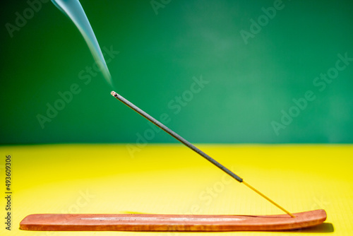 Smoky incense stick on yellow and green background.