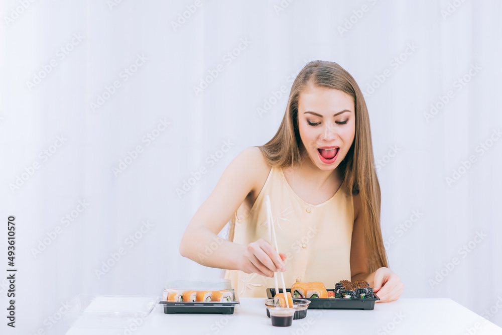A long-haired girl in a yellow jacket with an appetite eats sushi on a white background, a place for text