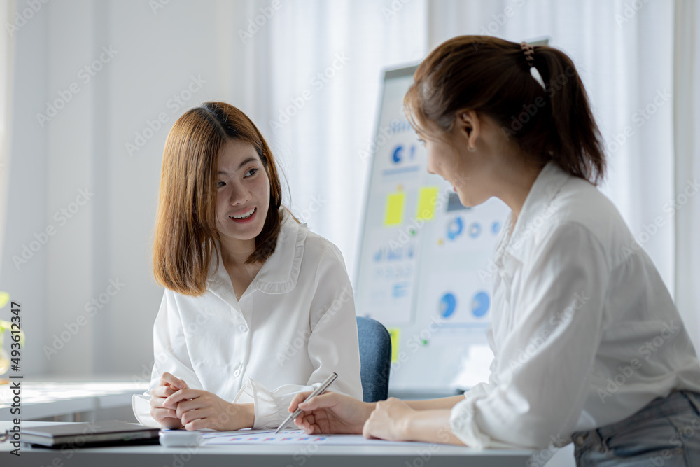 Two women sitting through white papers and talking, two business women discussing brainstorming and planning operations, form a partnership to form a startup company. Management of startup company. Two women sitting through white papers and talking, two business women discussing brainstorming and planning operations, form a partnership to form a startup company. Management of startup company.