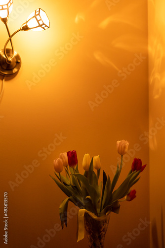 Bouquet of tulips on the bed-side table in the light of sconces in bedroom