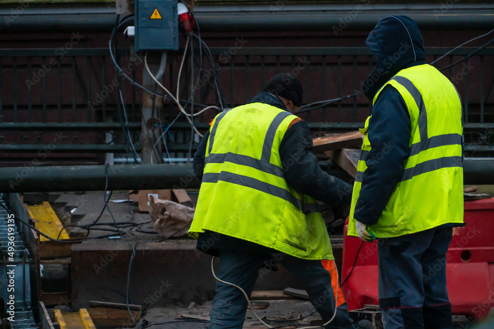 Employees of the road service in special yellow vests perform work on the repair of the roadway. Restoration of the deformation seam of the automobile bridge. Employees of the road service in special yellow vests perform work on the repair of the roadway. Restoration of the deformation seam of the automobile bridge.